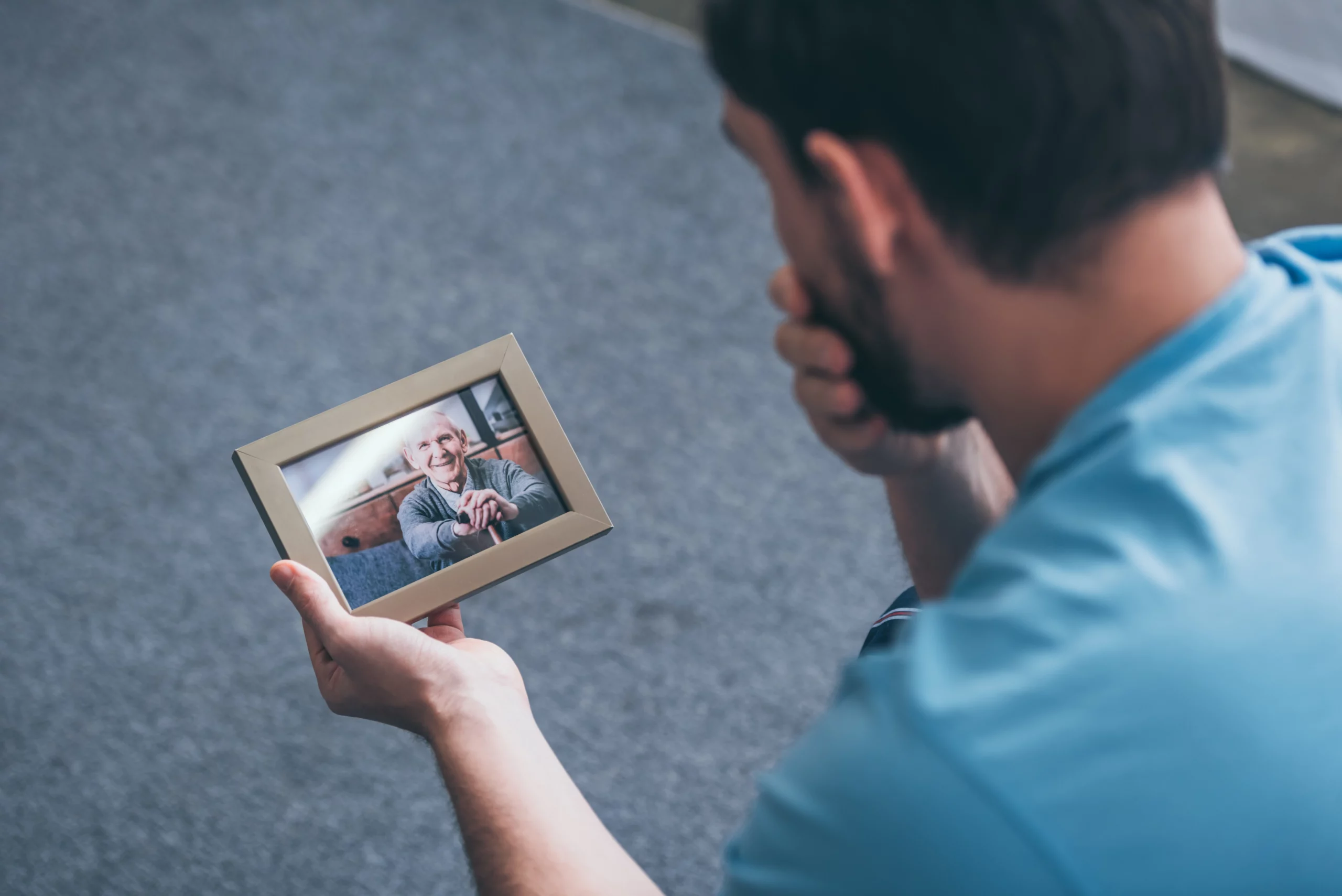 Man in blue shirt holding a framed photo of a smiling elderly man, reflecting on loss and the emotional toll of wrongful death.