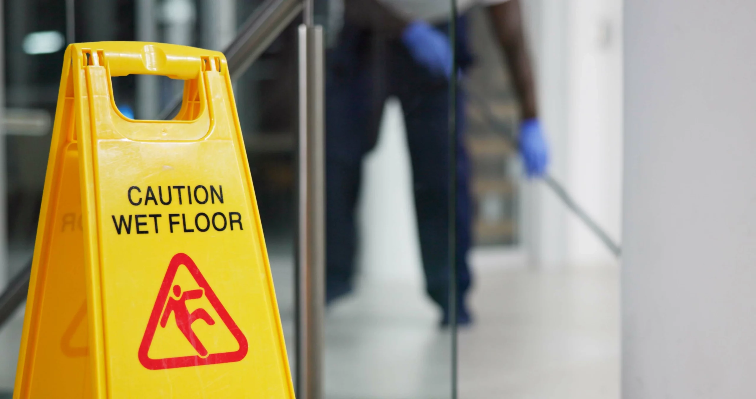 Wet floor caution sign in upscale retail store with cleaner mopping in background.