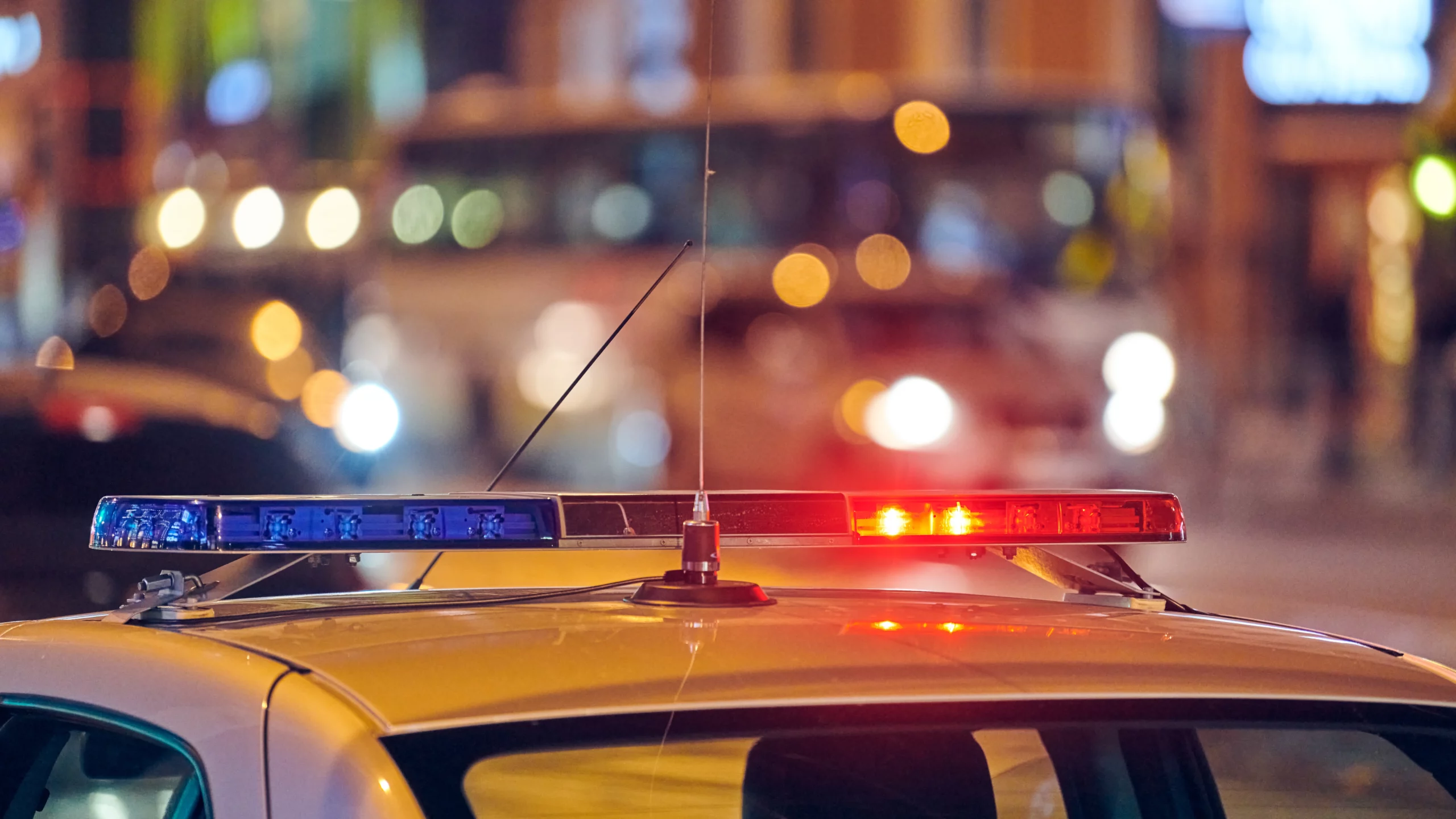 Flashing red and blue police lights atop a vehicle, illuminating a blurred city street at night, symbolizing law enforcement presence and urgency.